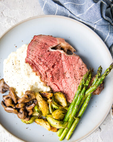 A smoked prime rib roast, perfectly medium rare, served with mashed potatoes, asparagus, and other veggies.