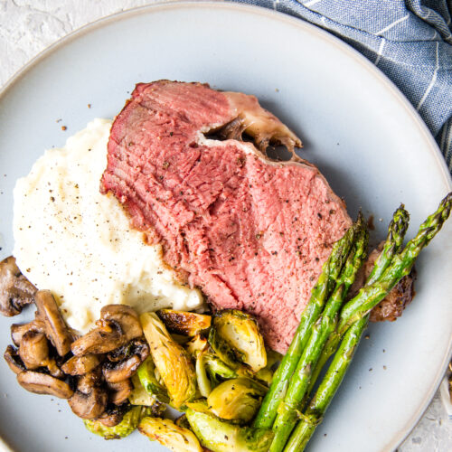 A smoked prime rib roast, perfectly medium rare, served with mashed potatoes, asparagus, and other veggies.