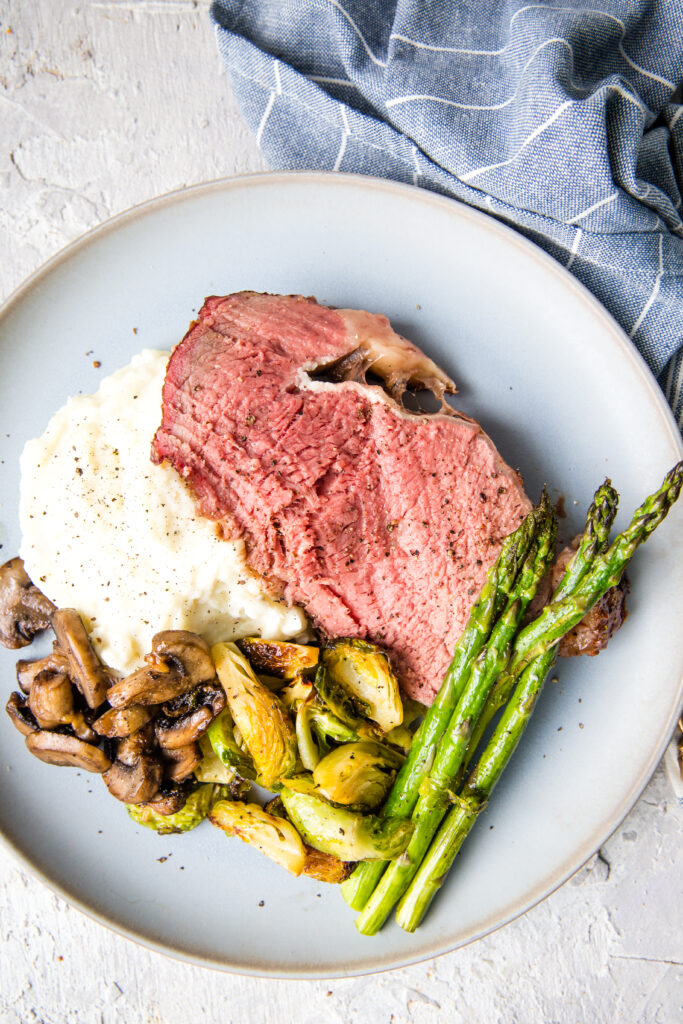 A smoked prime rib roast, perfectly medium rare, served with mashed potatoes, asparagus, and other veggies.