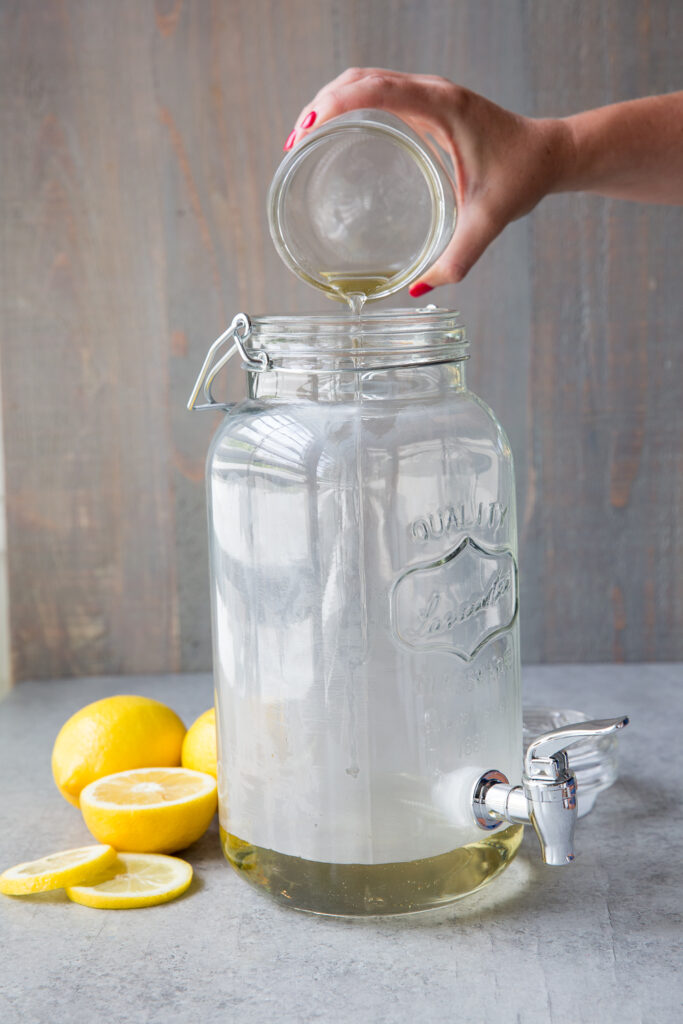 Pouring simple syrup into a drink dispenser to make homemade lemonade