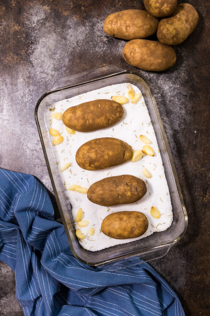 Salt baked potatoes, a baking dish with garlic, potatoes, salt, and rosemary