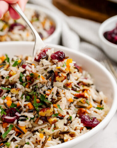 Wild rice pilaf in a white serving bowl, being served with a spoon