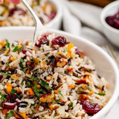 Wild rice pilaf in a white serving bowl, being served with a spoon