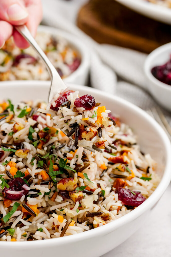 Wild rice pilaf in a white serving bowl, being served with a spoon
