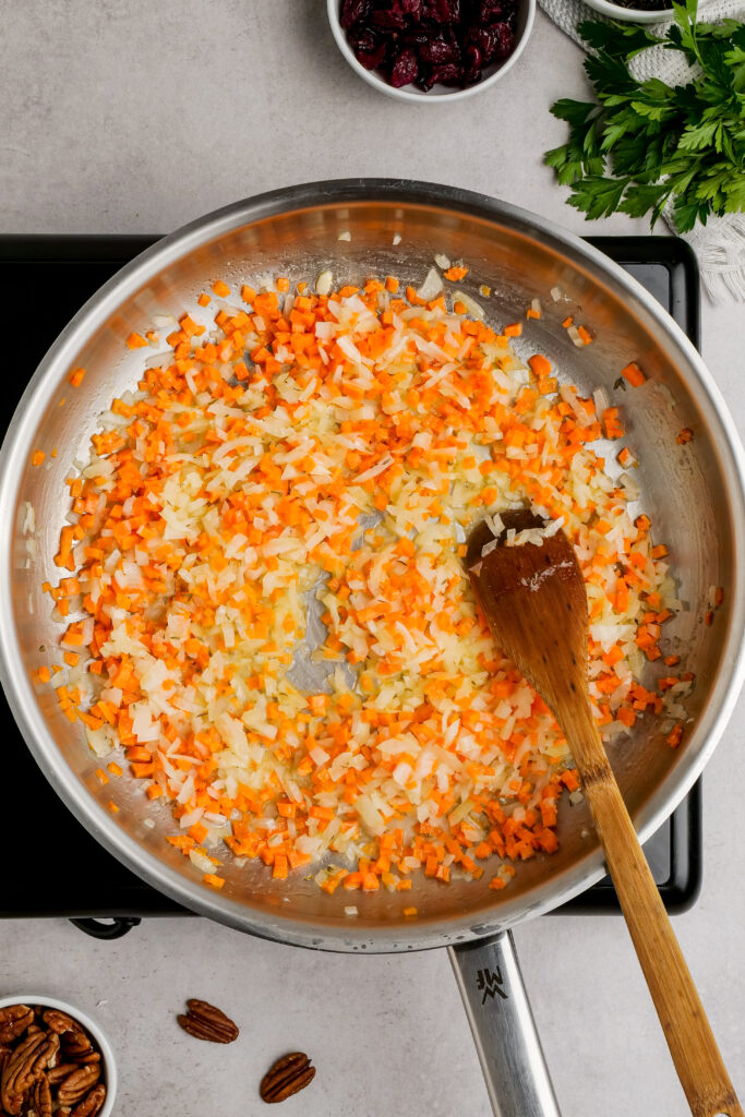 Cooking onions and carrots in a saucepan to make wild rice pilaf