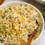 A white bowl with a spoon and herbed rice pilaf, a delightful rice pilaf with fresh herbs stirred in.