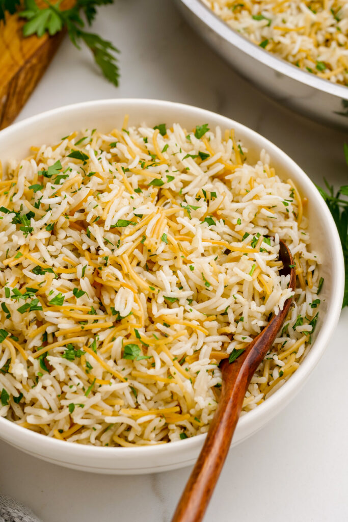 Herbed Rice Pilaf: A white bowl with a spoon and herbed rice pilaf, a delightful rice pilaf with fresh herbs stirred in. 