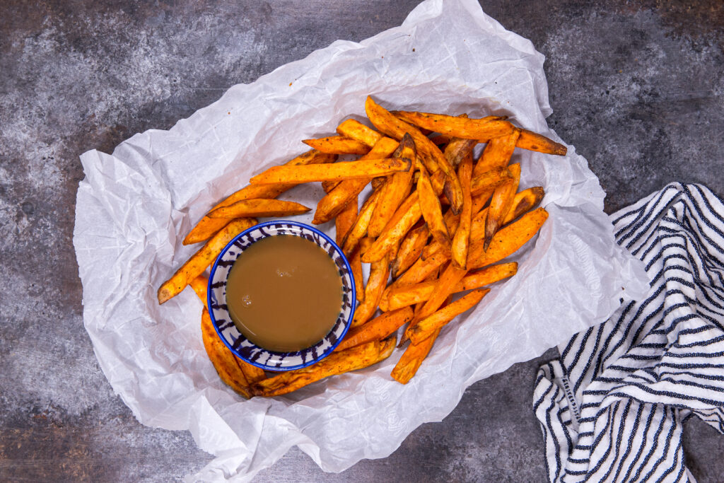 Crispy sweet potato fries in a basket with a caramel dipping sauce. 