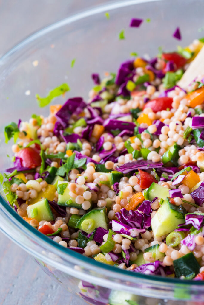 Couscous salad in a glass bowl, loaded with vegetables, pearl couscous, and flavor. 