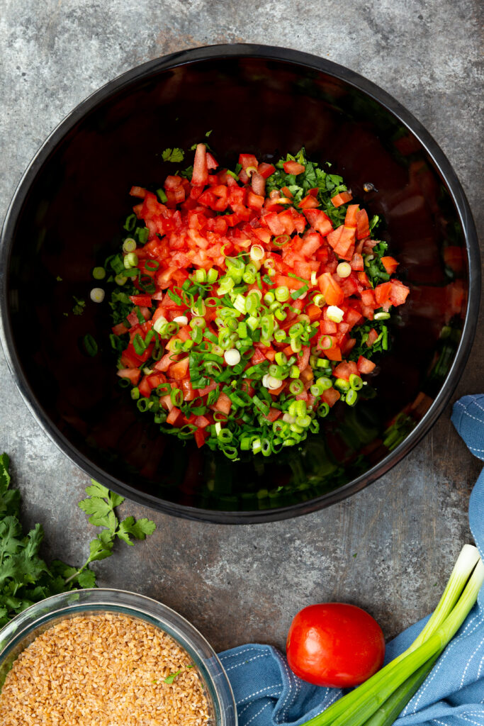 Combining the ingredients for an Israeli tabbouleh salad in a black bowl