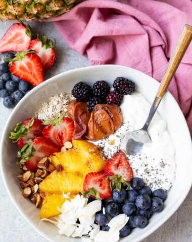 A cottage cheese breakfast bowl with grilled fruit and berries, oats, coconut, nuts, and chia seeds.