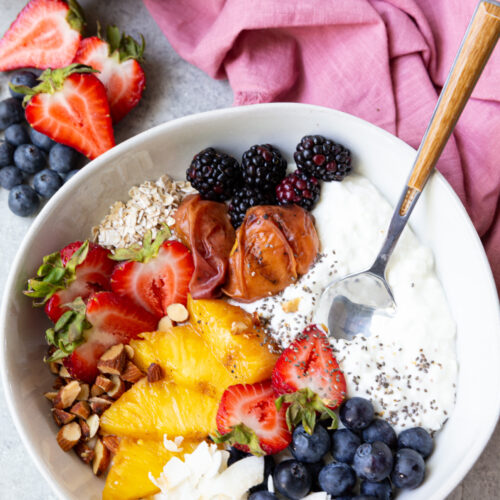 A cottage cheese breakfast bowl with grilled fruit and berries, oats, coconut, nuts, and chia seeds.
