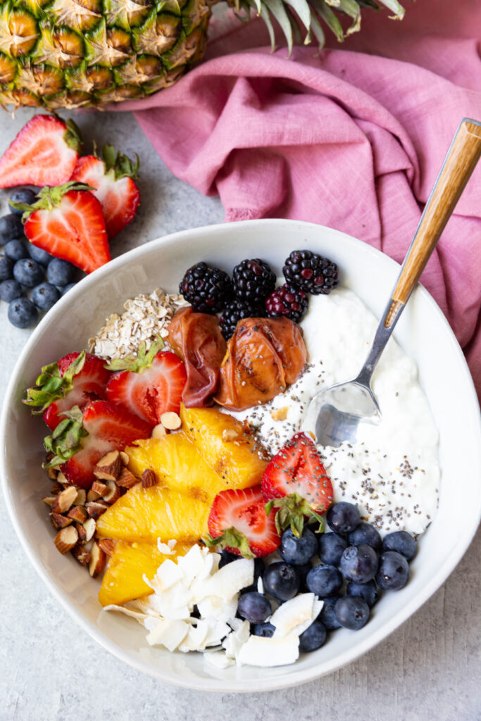 A cottage cheese breakfast bowl with grilled fruit and berries, oats, coconut, nuts, and chia seeds. 