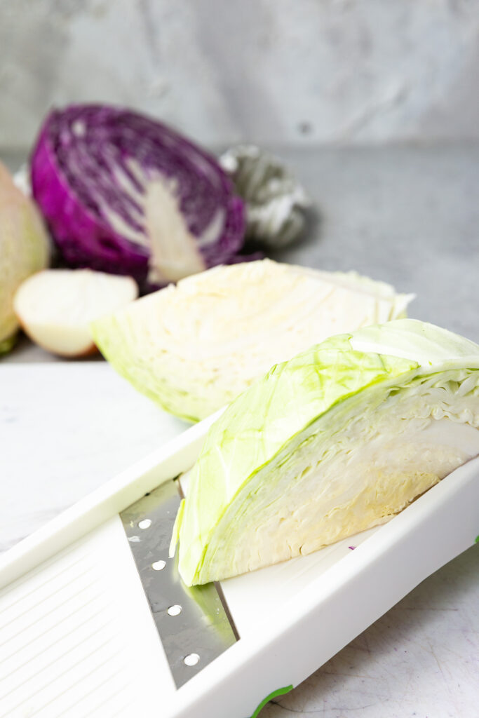 Cabbage being sliced in a mandoline slicer. 