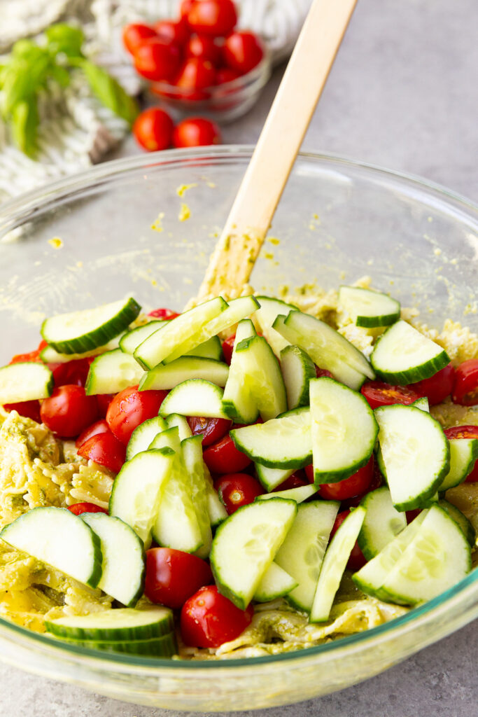 Mixing together a pesto pasta salad after adding fresh tomato and cucumber