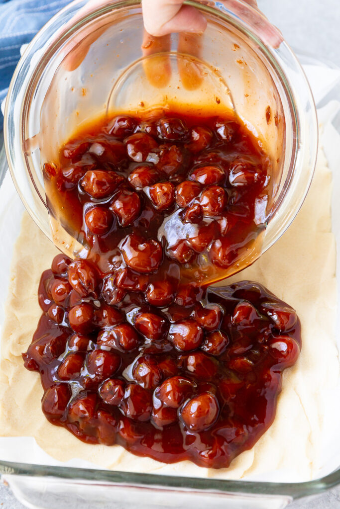 Topping pie bar base with cherry pie filling. 