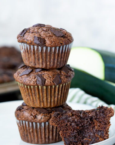 A stack of chocolate chunk zucchini muffins, with one cut open so you can see how rich and delicious it is.