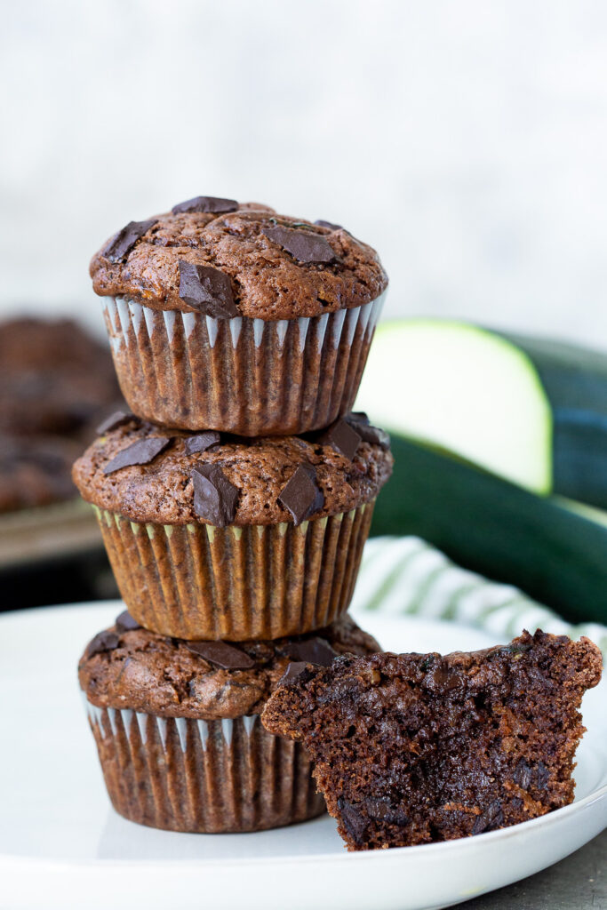 A stack of chocolate chunk zucchini muffins, with one cut open so you can see how rich and delicious it is. 