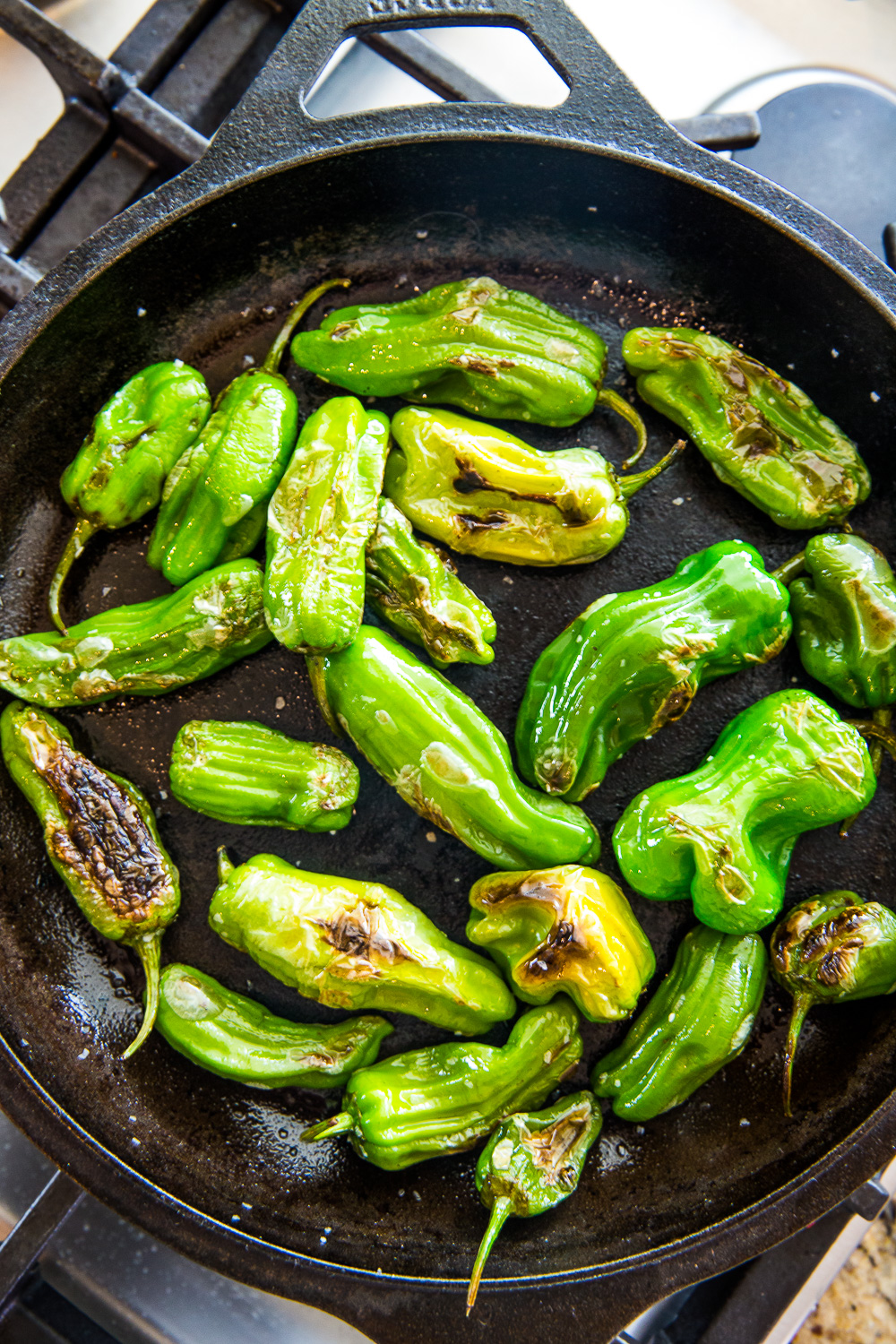 Blistered shishito peppers in a cast iron skillet