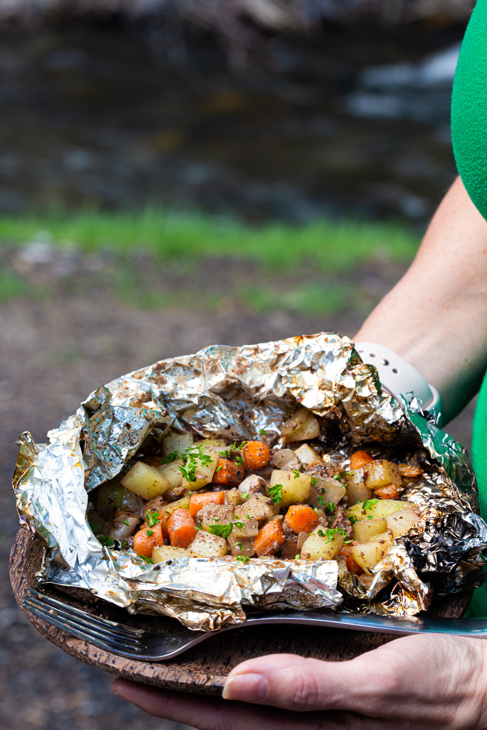 Foil dinners with hamburger and potatoes and carrots and onion, garnished with parsely. 