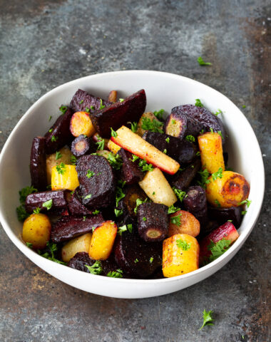 A bowl of roasted beets and carrots garnished with fresh parsley.