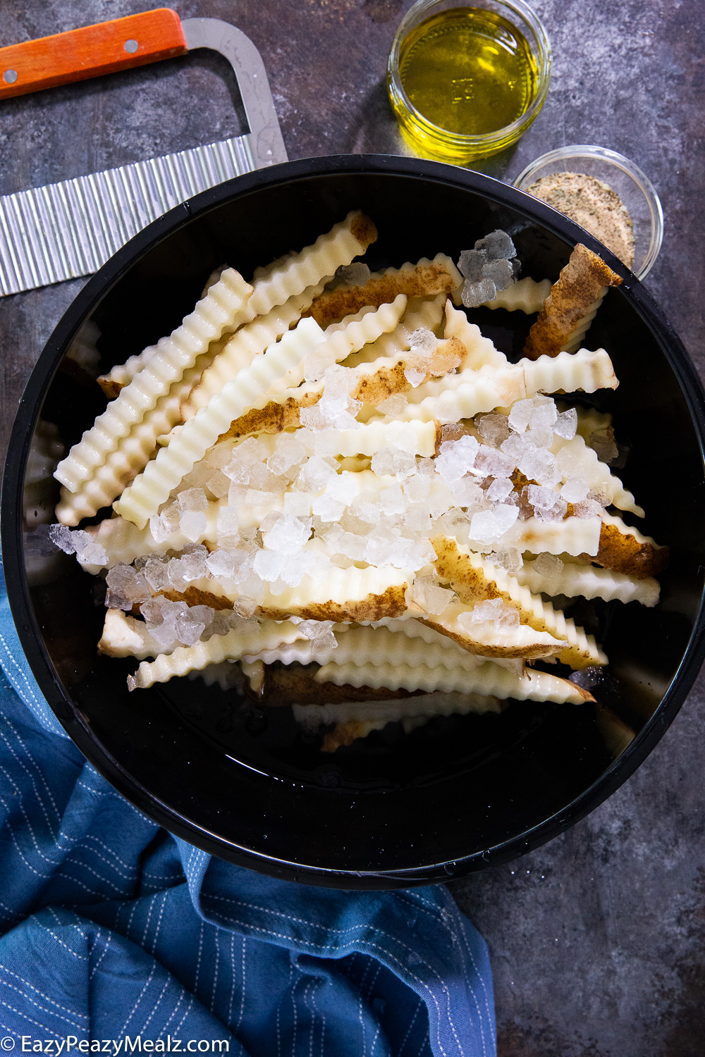 Crinkle cut fries, soaking in a bowl of water, ice, and salt. 