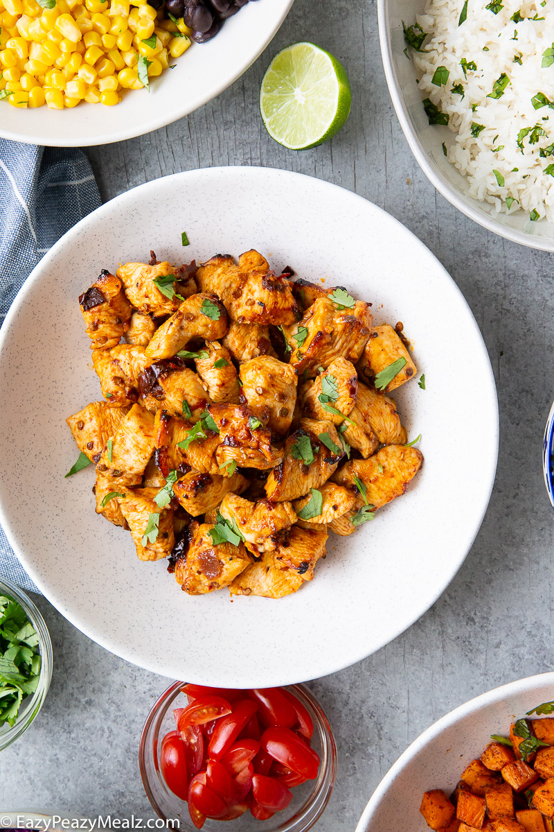 Hot honey chipotle chicken bites in a bowl, ready to be served with fixings for salads.