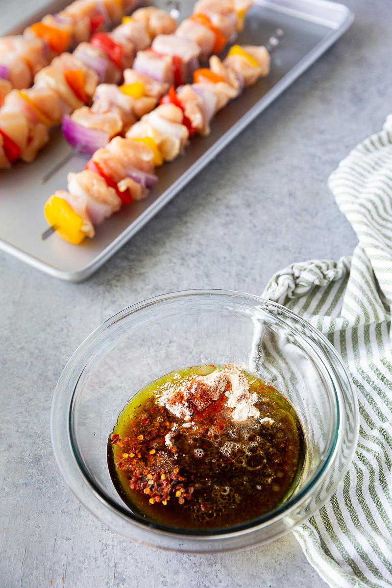 Bowl of chicken skewer marinade with skewered chicken and vegetables blurred in the background.
