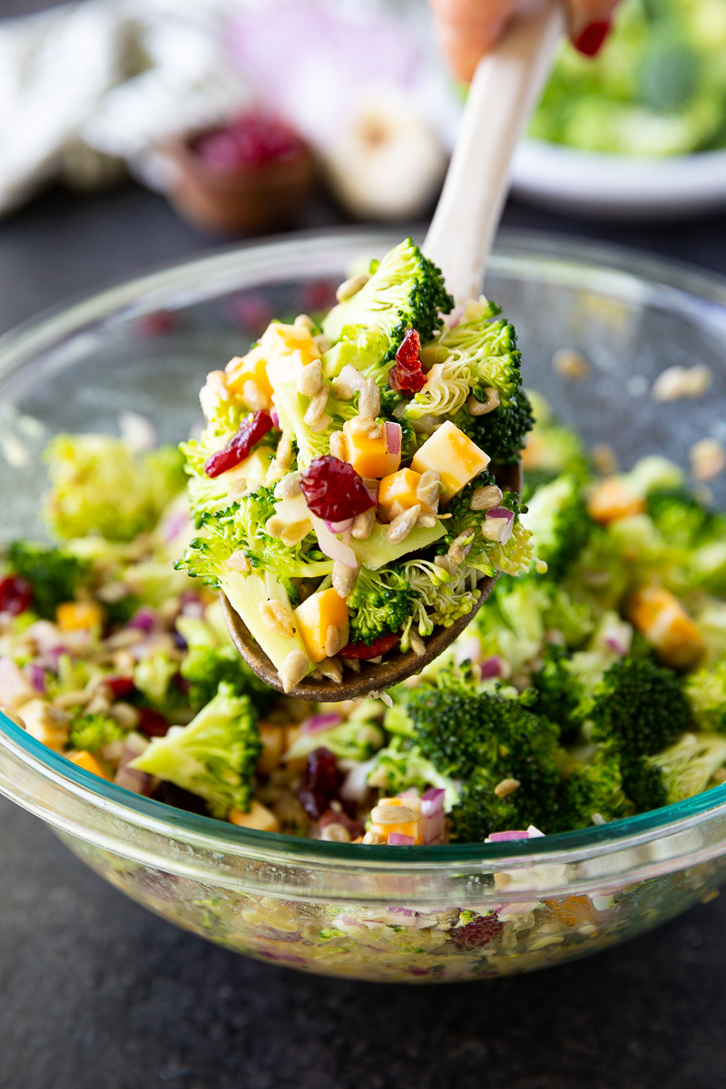 A vibrant bowl of broccoli salad featuring crisp florets, dried cranberries, sunflower seeds, red onion, and cheese cubes, all tossed in a tangy honey mustard dressing—fresh, colorful, and ready to serve.
