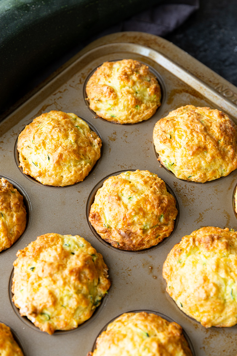 Freshly baked zucchini muffins cooling on a wire rack, with golden cheesy tops and a soft, veggie-packed interior.