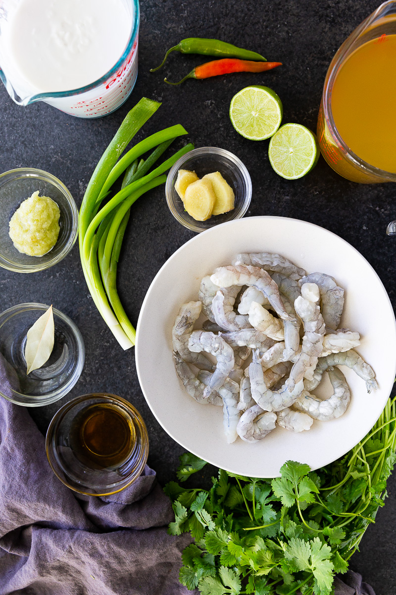Fresh ingredients for Tom Kha soup, including creamy coconut milk, tender shrimp, fragrant lemongrass, ginger, limes, mushrooms, chili, and cilantro for authentic Thai flavor.