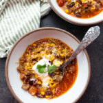 Two bowls of taco soup topped with sour cream, cheese, and cilantro.