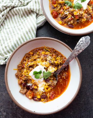 Two bowls of taco soup topped with sour cream, cheese, and cilantro.