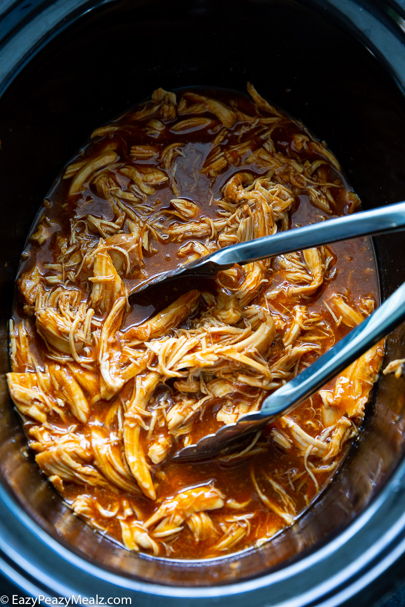 Crockpot full of tender, shredded zesty BBQ chicken, coated in smoky-sweet barbecue sauce and ready to serve.