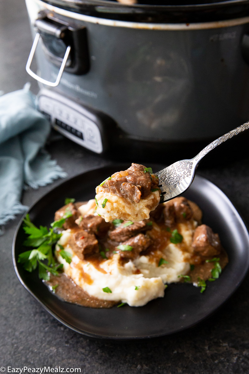 A fork full of slow cooker steak bites and mashed potatoes
