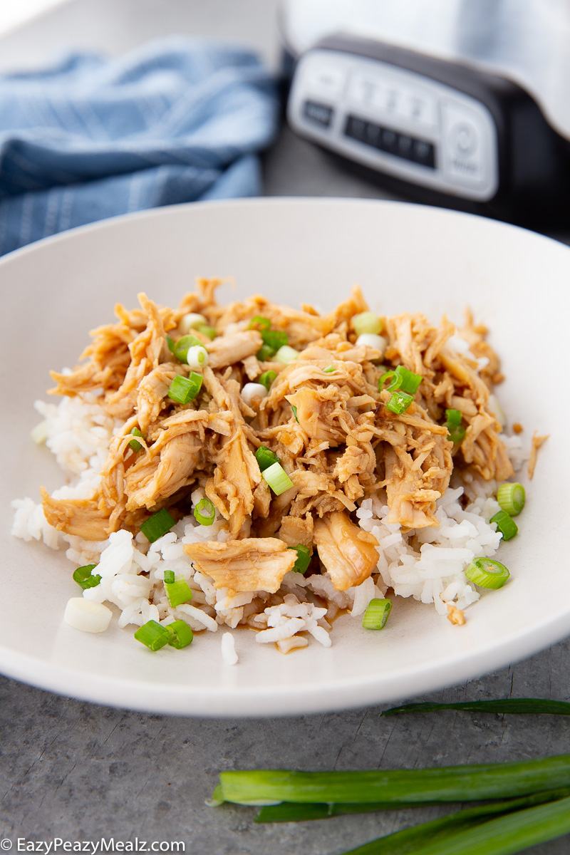 Slow cooker honey garlic chicken over white rice with sesame seeds and green onions