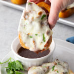 Texas toast french dip being dipped in au jus