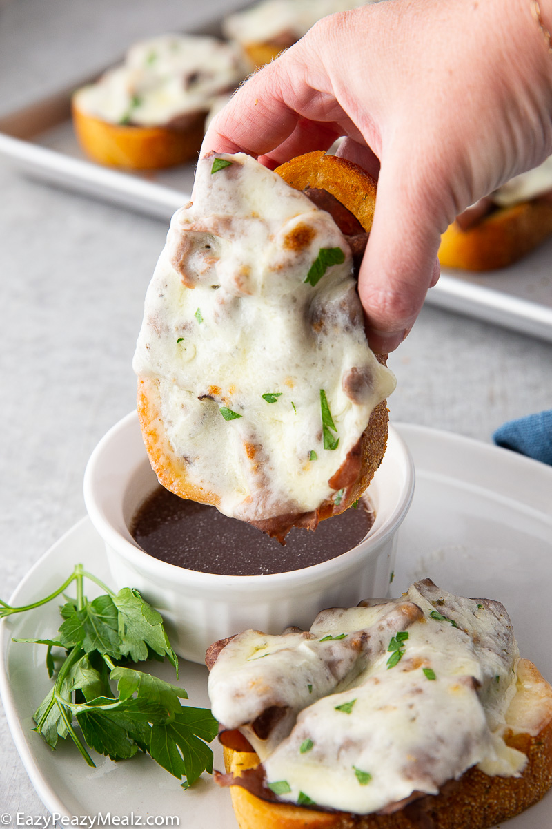 Texas toast french dip being dipped in au jus