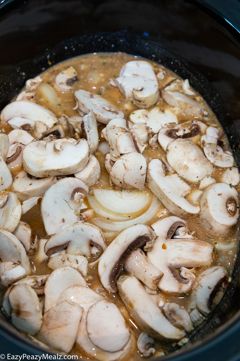 A slow cooker with everything in it to make creamy slow cooked pork chops in a mushroom gravy.